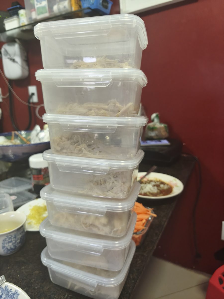 Torre de potes plásticos transparentes empilhados sobre a bancada, cada um com uma porção de frango desfiado, prontos para ir ao freezer.