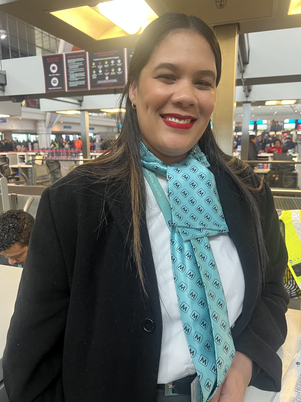 Lizelle Ziegelaar de uniforme da TAAG, com o lenço azul-turquesa da companhia, sorrindo no balcão de check-in do aeroporto