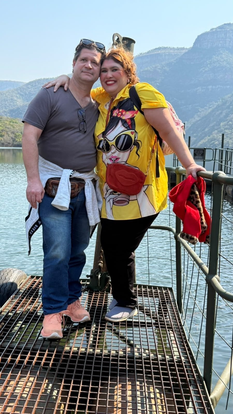 Diana e Nicco abraçados no atracadouro flutuante da represa do Blyde River Canyon, com a água e os paredões do cânion ao fundo.