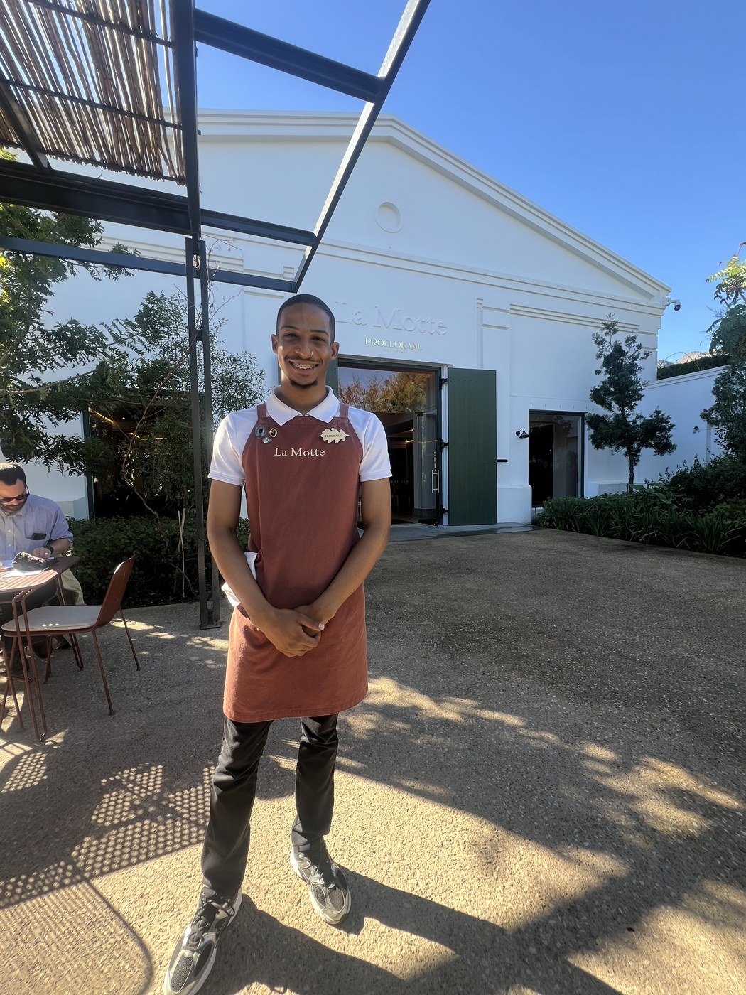 Terrence, de avental terracota da La Motte, em pé no pátio de entrada da vinícola, sorrindo