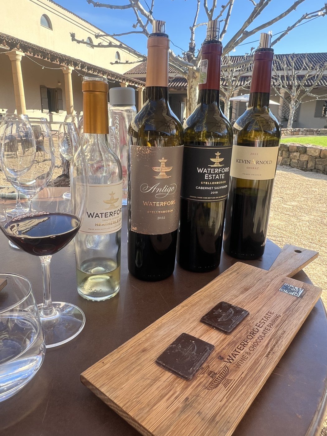 A tábua do Wine and Chocolate Pairing do Waterford Estate, com dois chocolates e as quatro garrafas atrás: Heatherleigh, Antigo 2022, Cabernet Sauvignon 2019 e Kevin Arnold Shiraz 2021