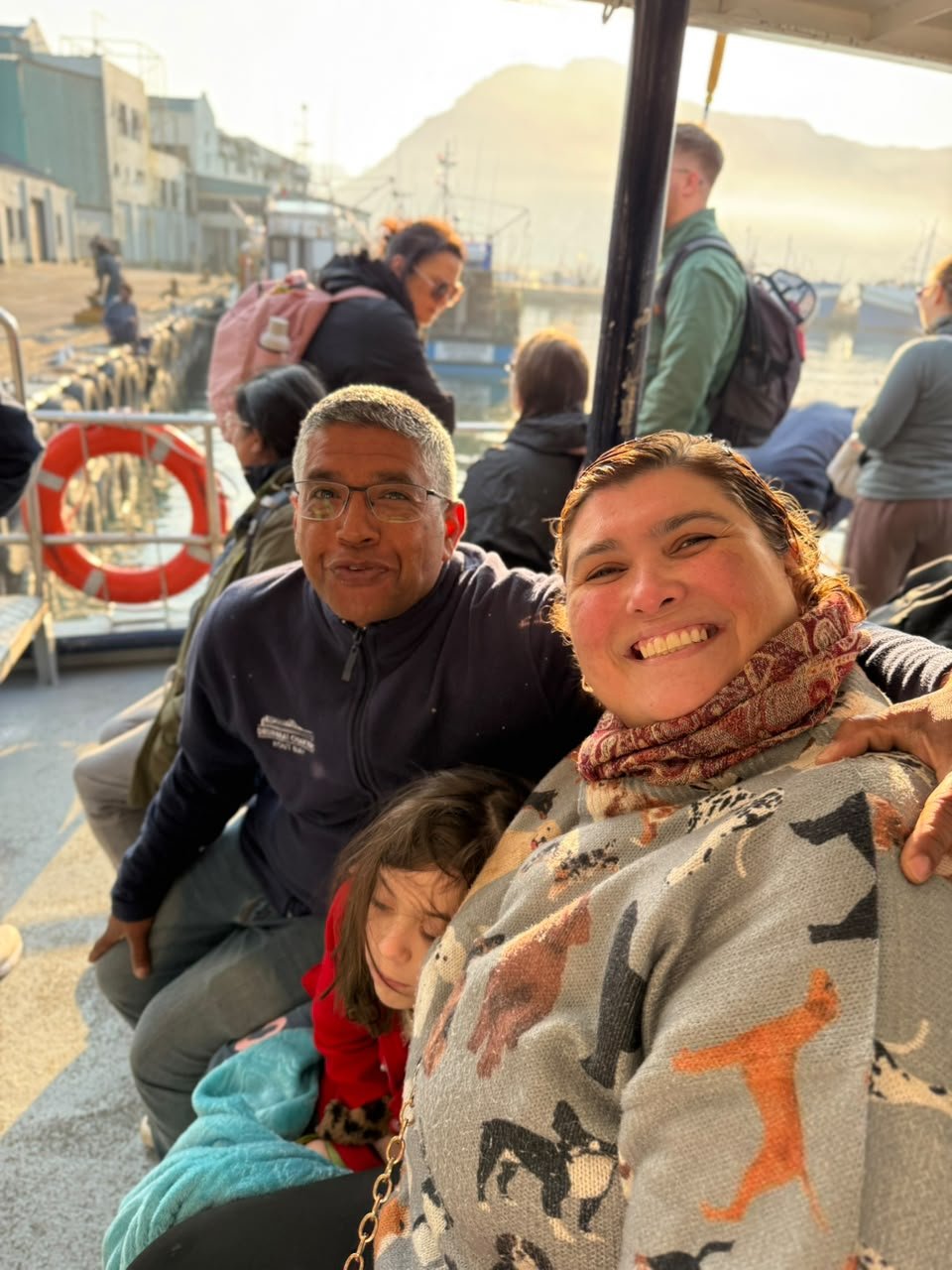Popeye, tripulante de casaco da Drumbeat Charters, sentado ao lado de Diana no barco em Hout Bay, com a Dinah dormindo entre elas coberta por um lençol