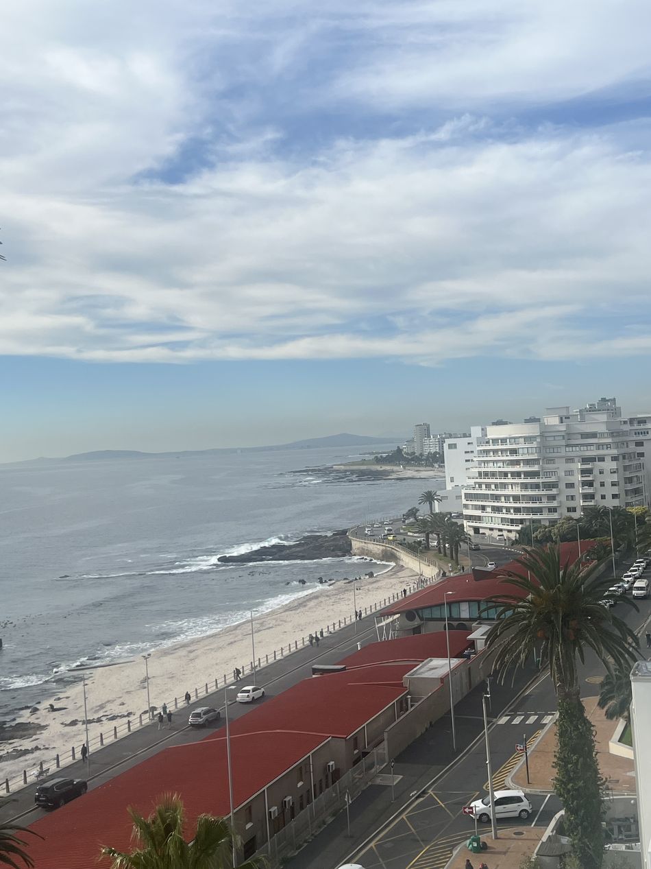A vista da janela do apartamento: o mar, a orla de Sea Point com o calçadão e a praia, os prédios brancos e a costa ao fundo